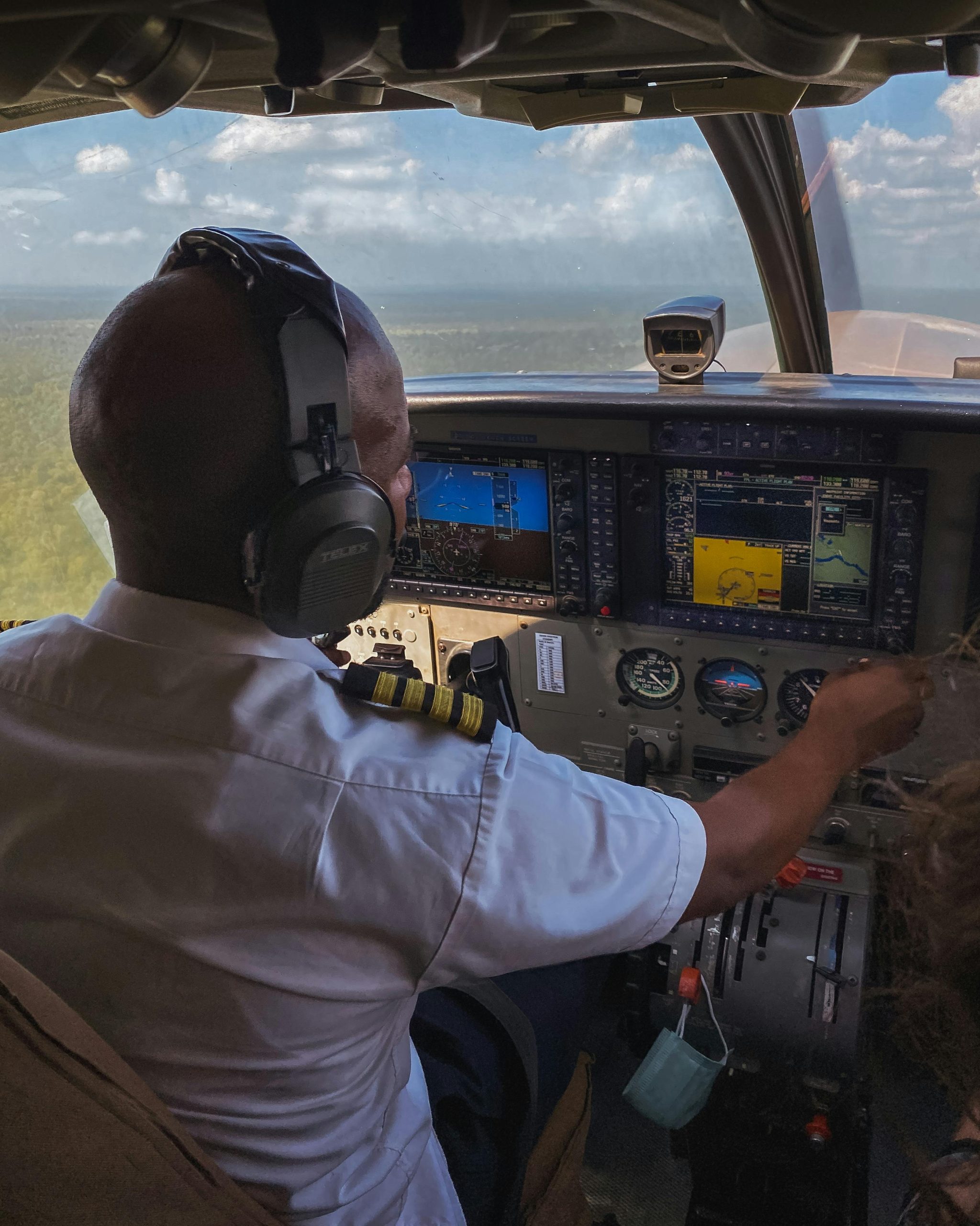 Pilot in cockpit flying over scenic Tanzania landscape, showcasing aviation prowess.